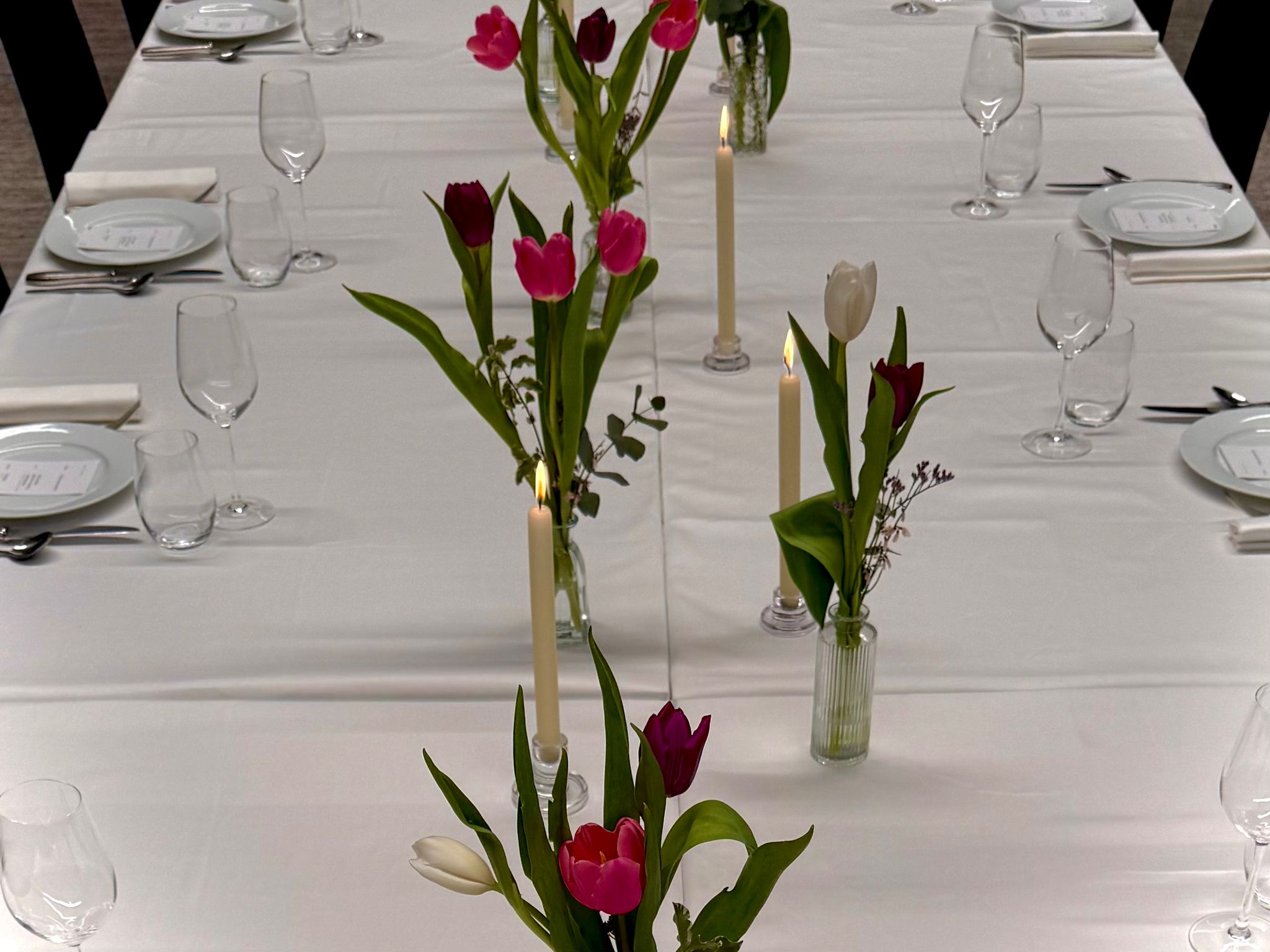Table dressée pour un dîner d'entreprise à Paris par NOCTA Catering — nappe blanche, tulipes fraîches, bougies allumées, couverts haut de gamme