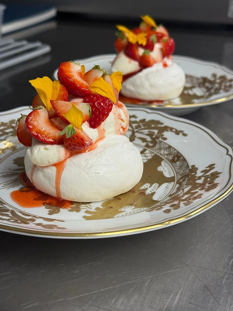 Pavlova fraise et fleurs comestibles sur porcelaine — dessert traiteur NOCTA Paris